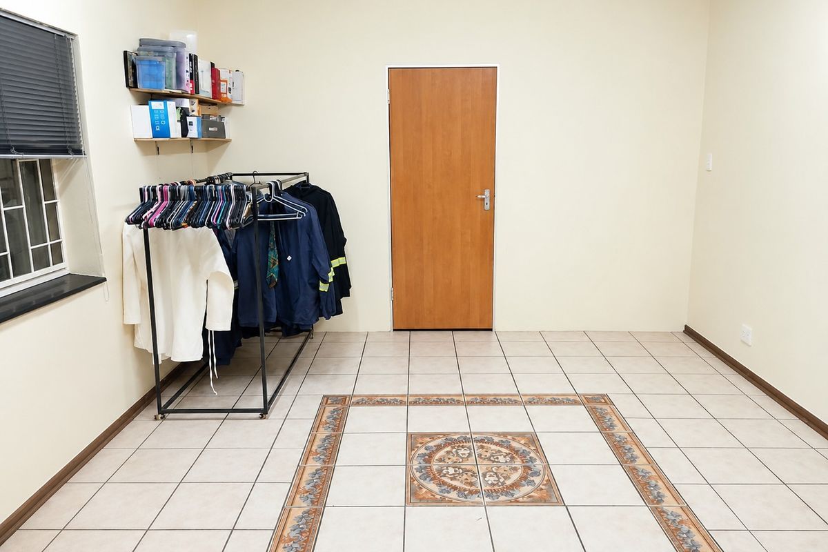 A spacious, neutrally painted bedroom featuring tiled flooring with a decorative central inlay and a secure window.