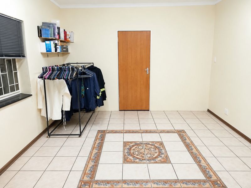 A spacious, neutrally painted bedroom featuring tiled flooring with a decorative central inlay and a secure window.