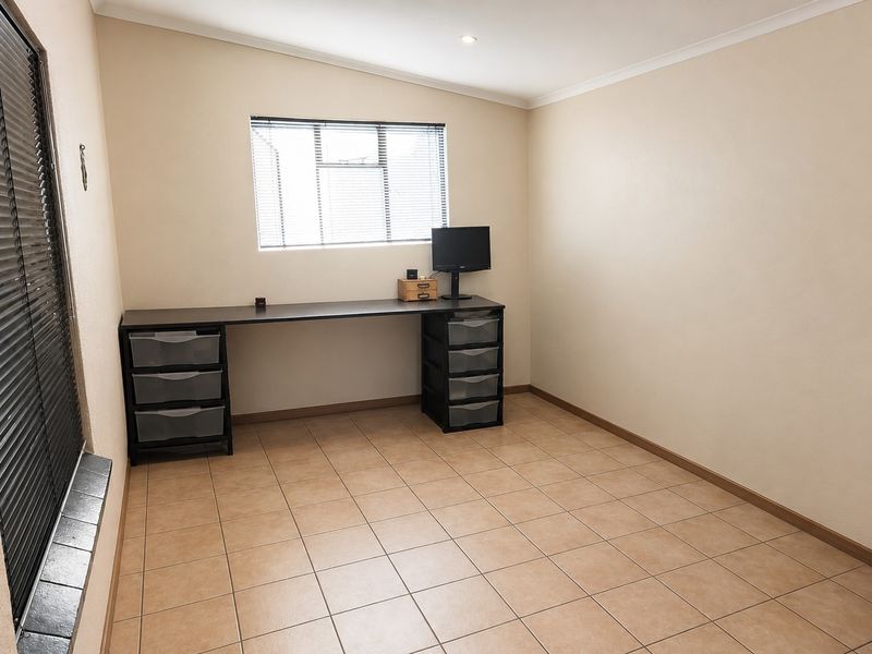 A functional office space featuring neutral wall tones, tiled flooring, and venetian blinds, providing a clean and versatile area for work or study.