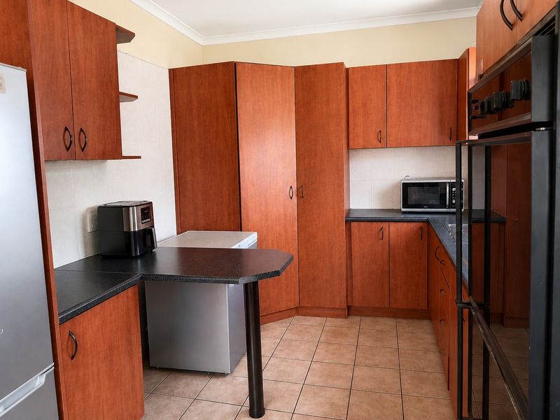 A functional kitchen featuring warm-toned wooden cabinetry, dark laminate countertops, tiled flooring, and a built-in oven, offering ample storage and workspace.