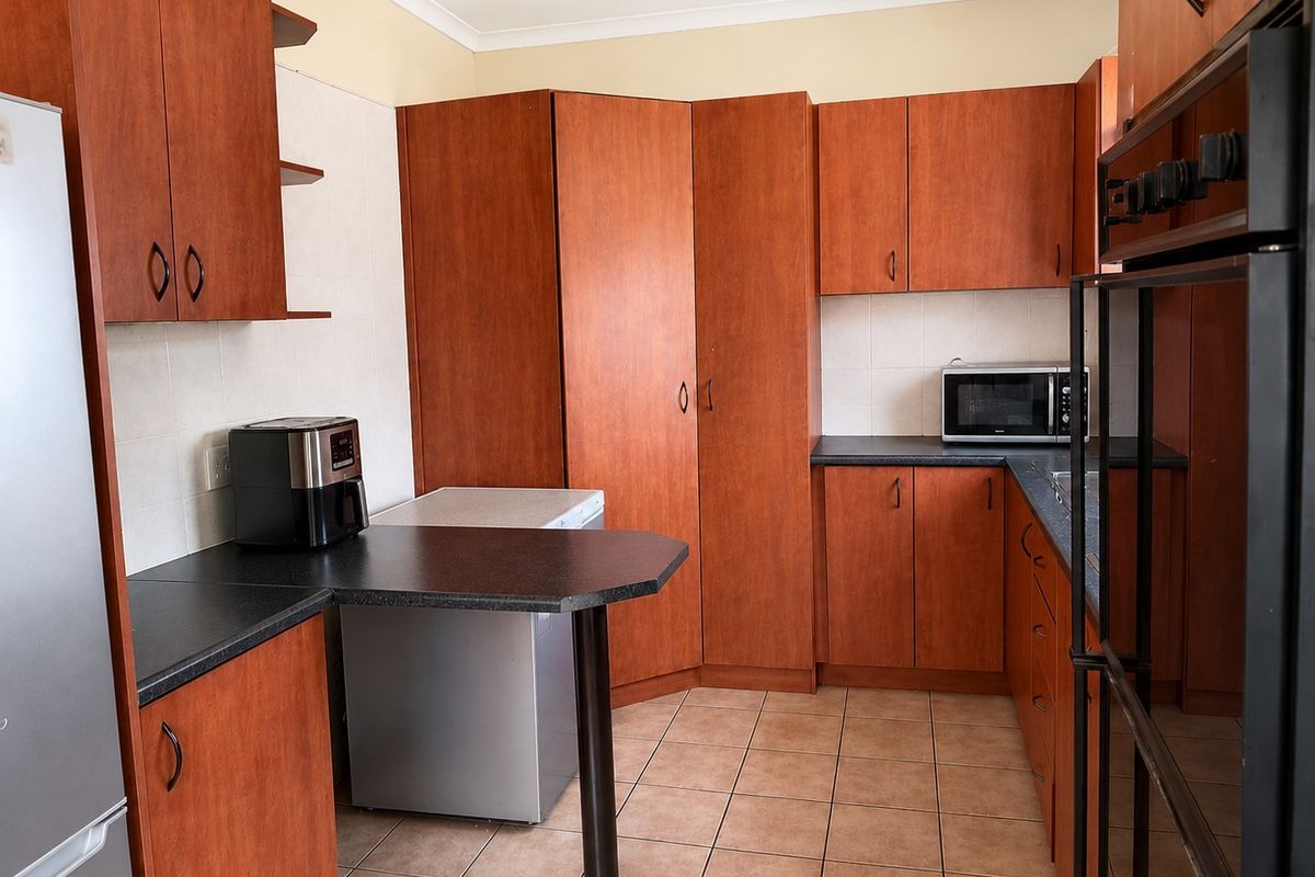 A functional kitchen featuring warm-toned wooden cabinetry, dark laminate countertops, tiled flooring, and a built-in oven, offering ample storage and workspace.