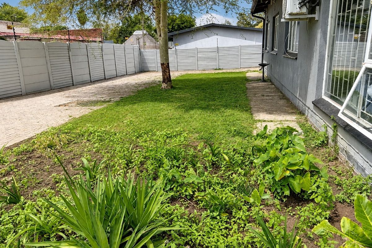 Rear garden area featuring a paved section, lawn, and perimeter precast concrete walling, with an exterior air conditioning unit mounted on the house wall.