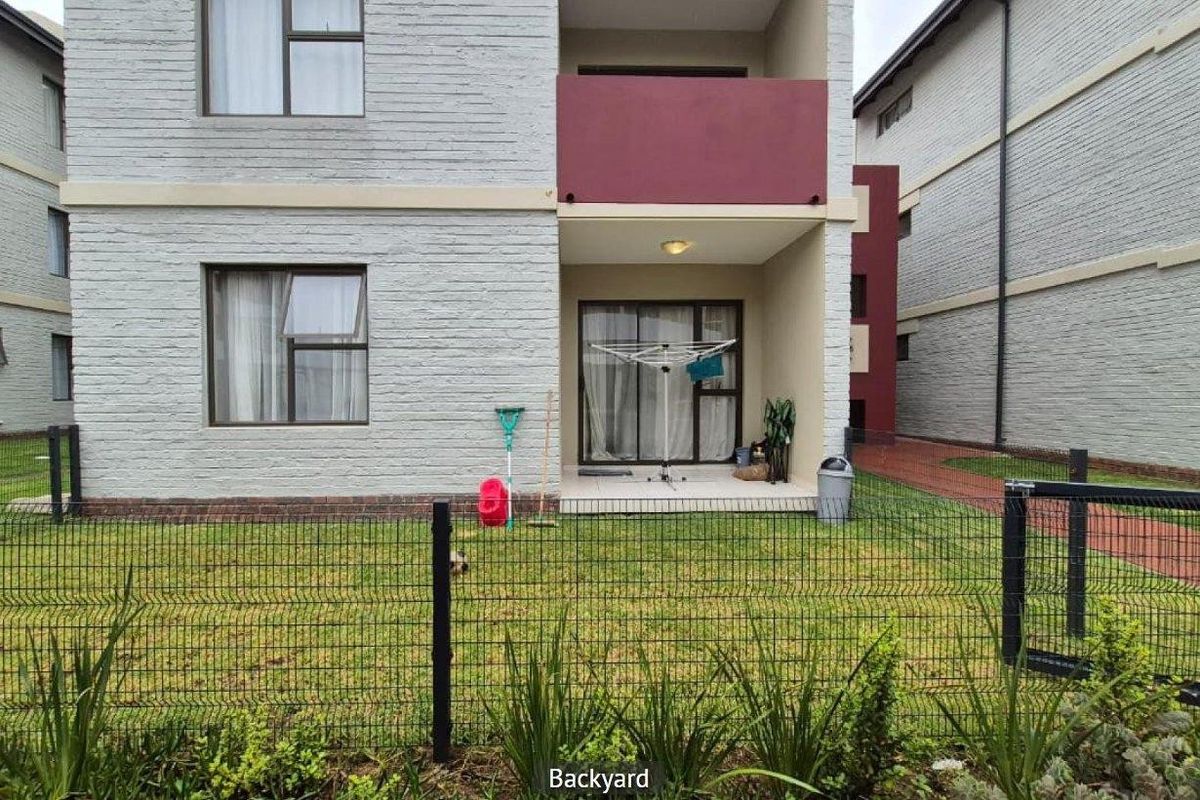 Rear view of the apartment building featuring a ground floor patio area, sliding glass doors, and a private fenced garden space.