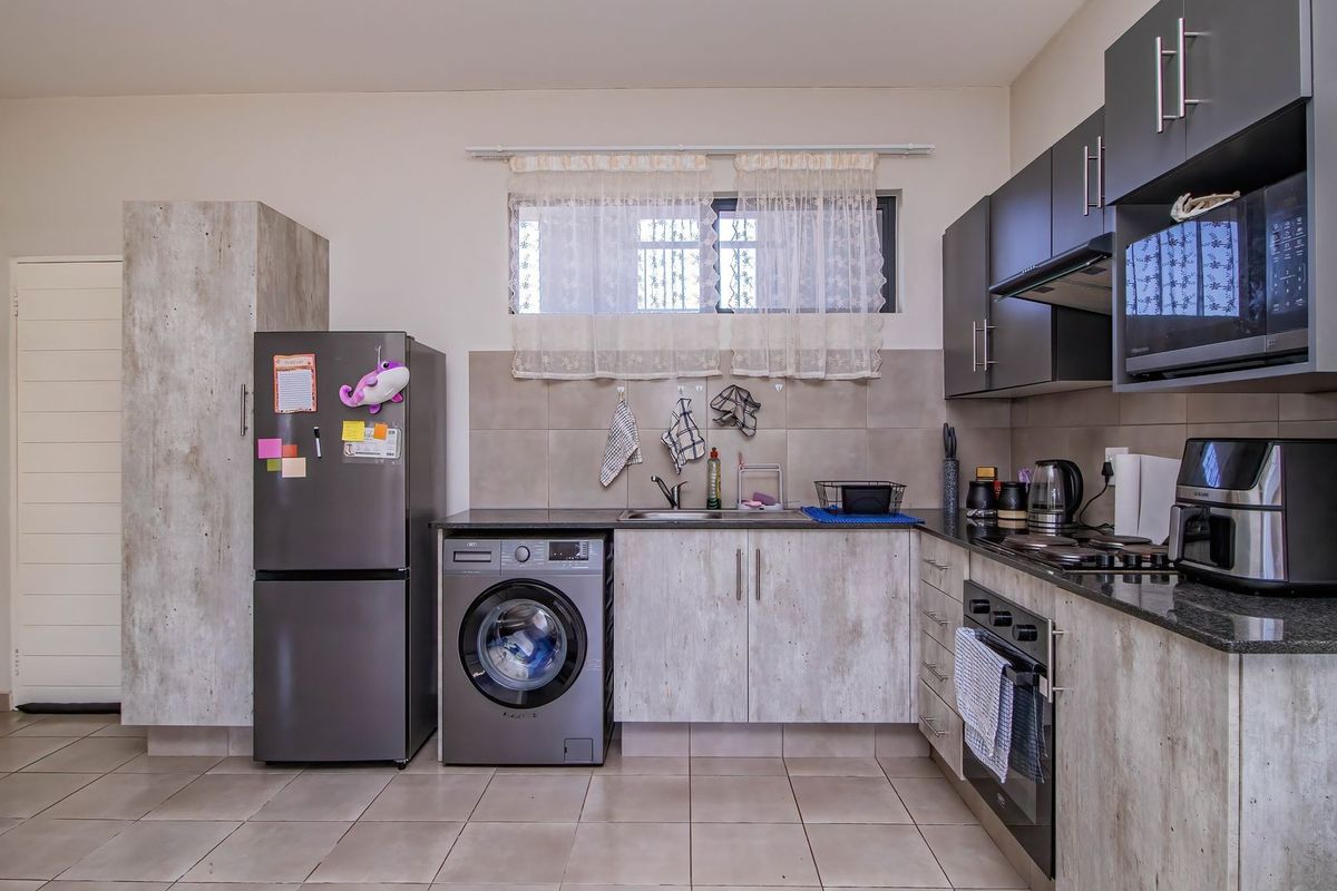 A functional kitchen featuring dark cabinetry, granite countertops, a built-in oven, hob, and integrated laundry space with tiled flooring.