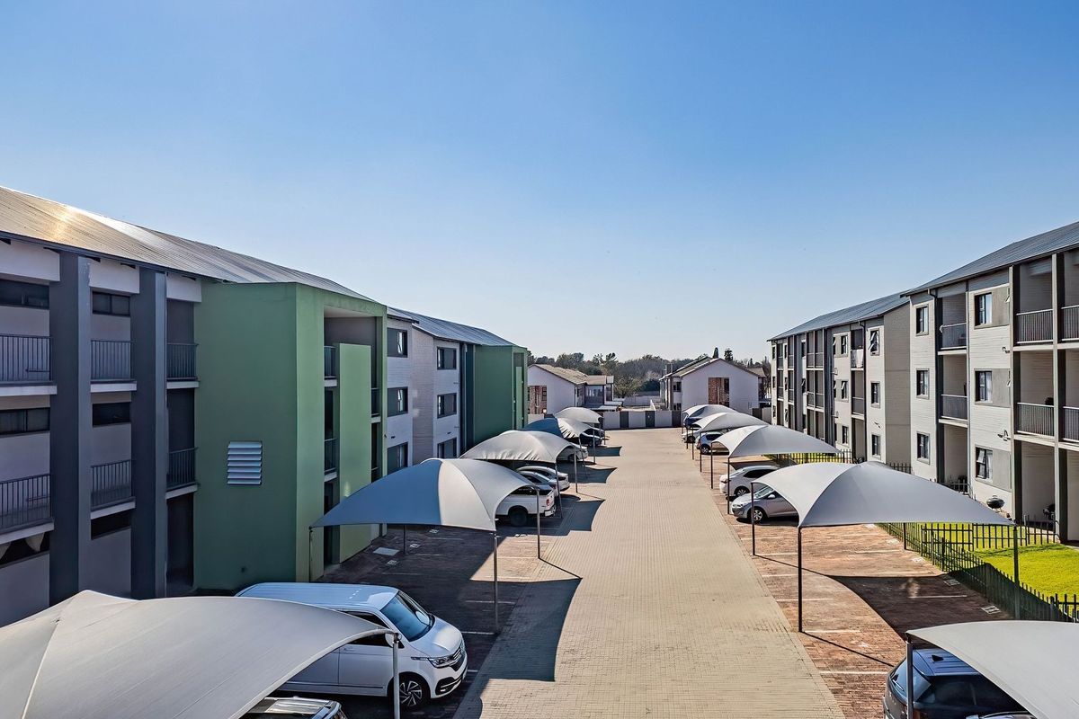 Exterior view of an apartment complex featuring paved parking areas with shade-cloth carports between the residential buildings.