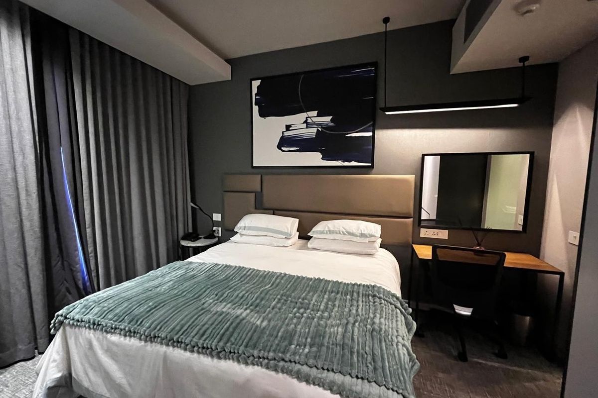 A modern bedroom featuring a built-in upholstered headboard, integrated desk area, and contemporary pendant lighting in a neutral, sophisticated color palette.