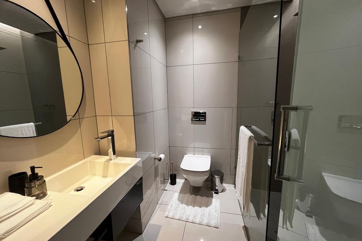 Modern bathroom featuring a wall-mounted toilet, sleek vanity with integrated basin, and a glass-enclosed shower with contemporary tiling.
