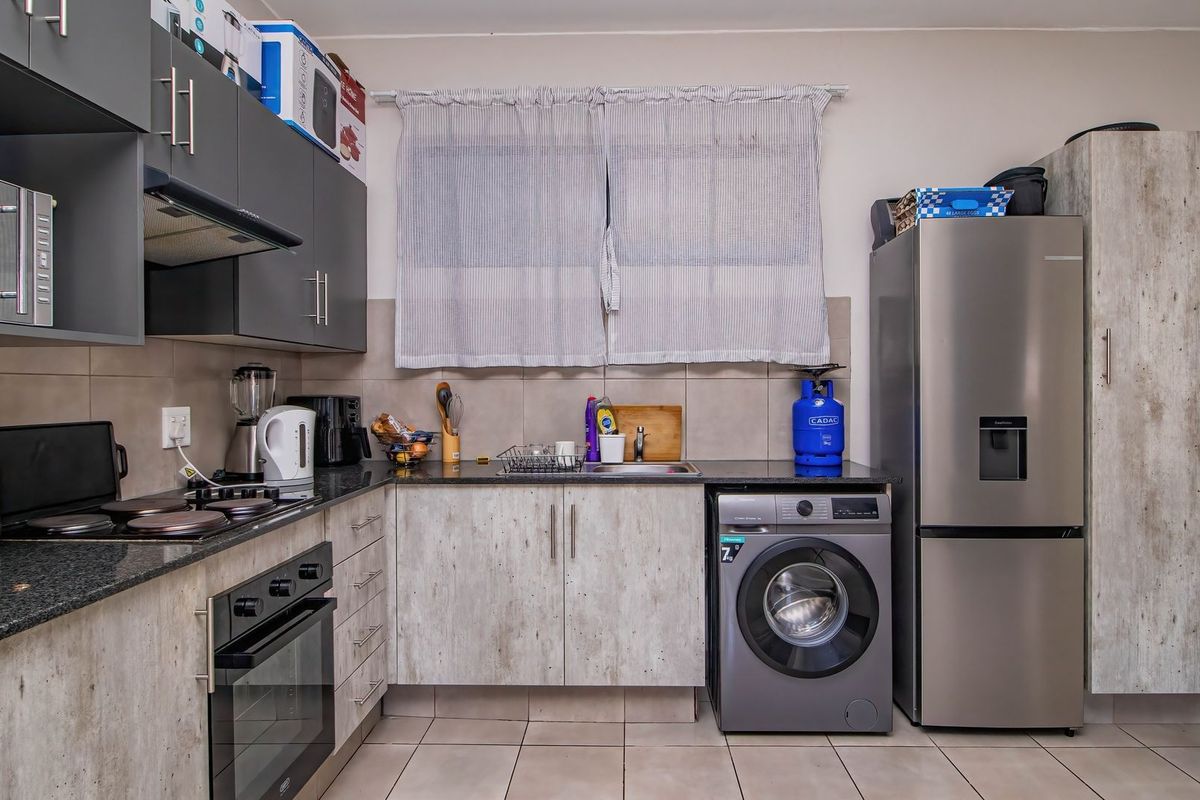 A functional kitchen featuring modern grey cabinetry, granite countertops, a built-in oven, hob, extractor fan, and integrated space for a washing machine.