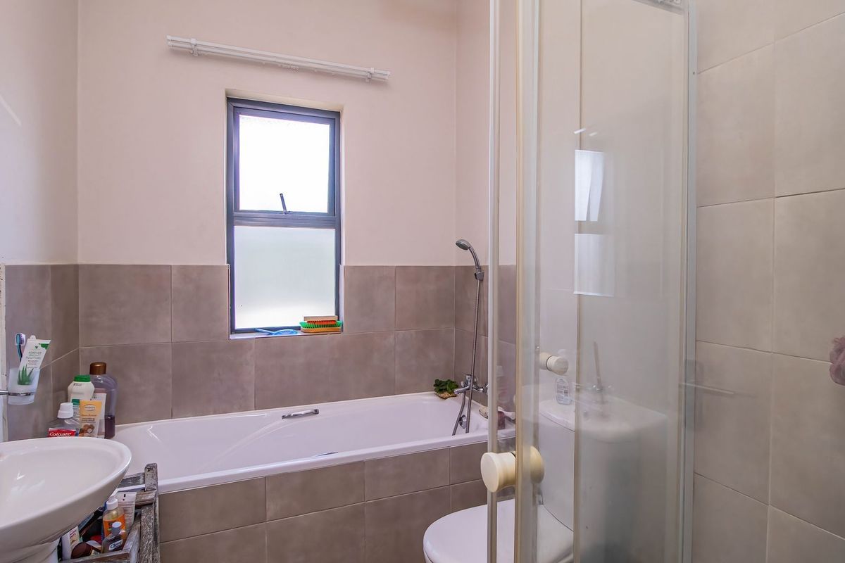 A functional bathroom featuring a combined bathtub and shower unit, a pedestal sink, and neutral wall tiling.