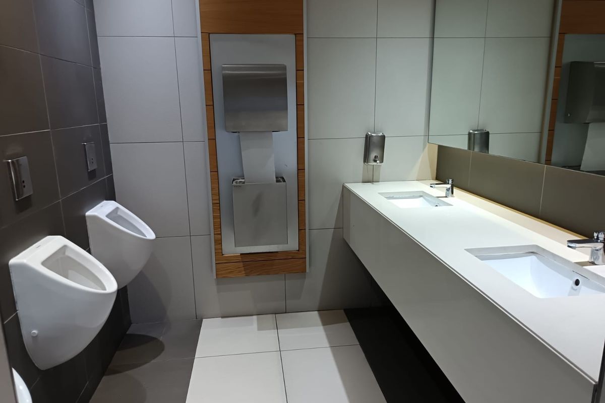 Modern commercial restroom featuring wall-mounted urinals, a sleek double vanity with integrated sinks, and stainless steel fixtures.