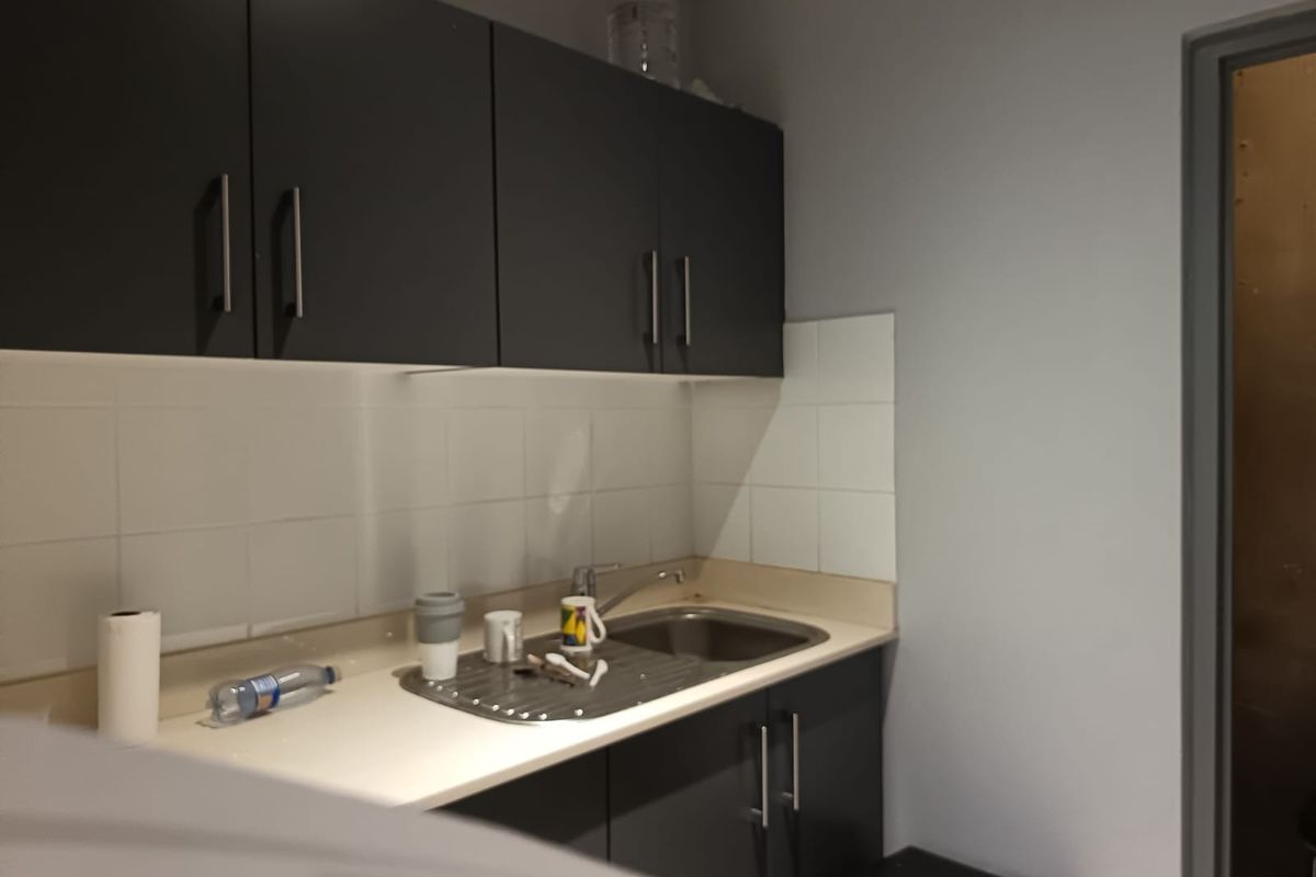 A compact kitchenette featuring dark cabinetry, a stainless steel sink, and white tiled splashback, suitable for office or utility use.