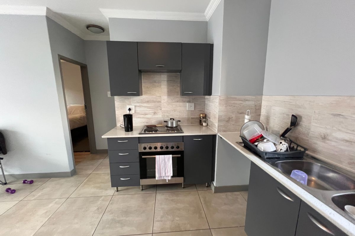 Compact kitchen featuring dark grey cabinetry, light stone-look countertops, tiled backsplash, and a built-in oven with a gas hob.