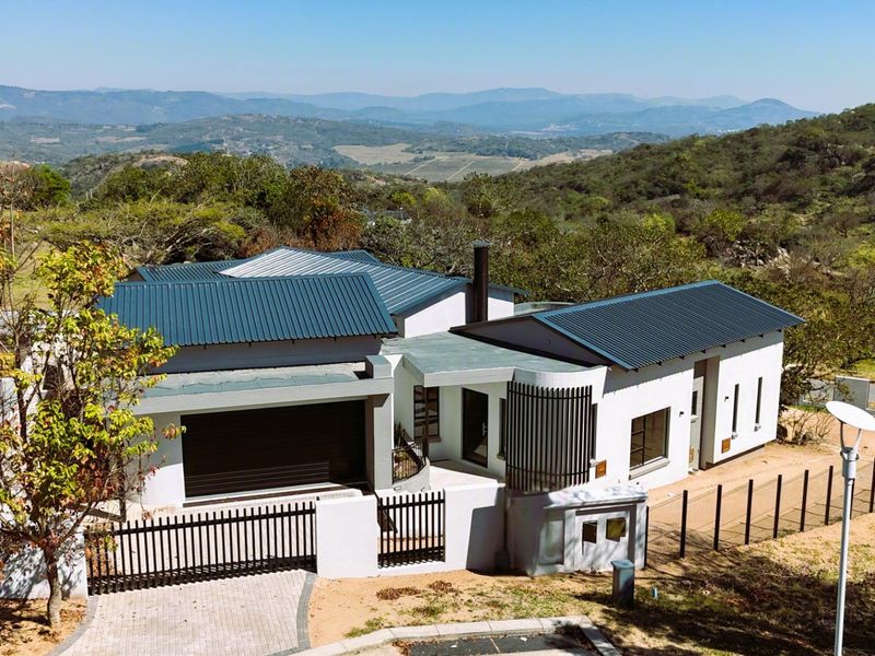 Aerial view of a modern residence featuring a corrugated metal roof, double garage, and paved driveway, set against a scenic mountainous landscape.