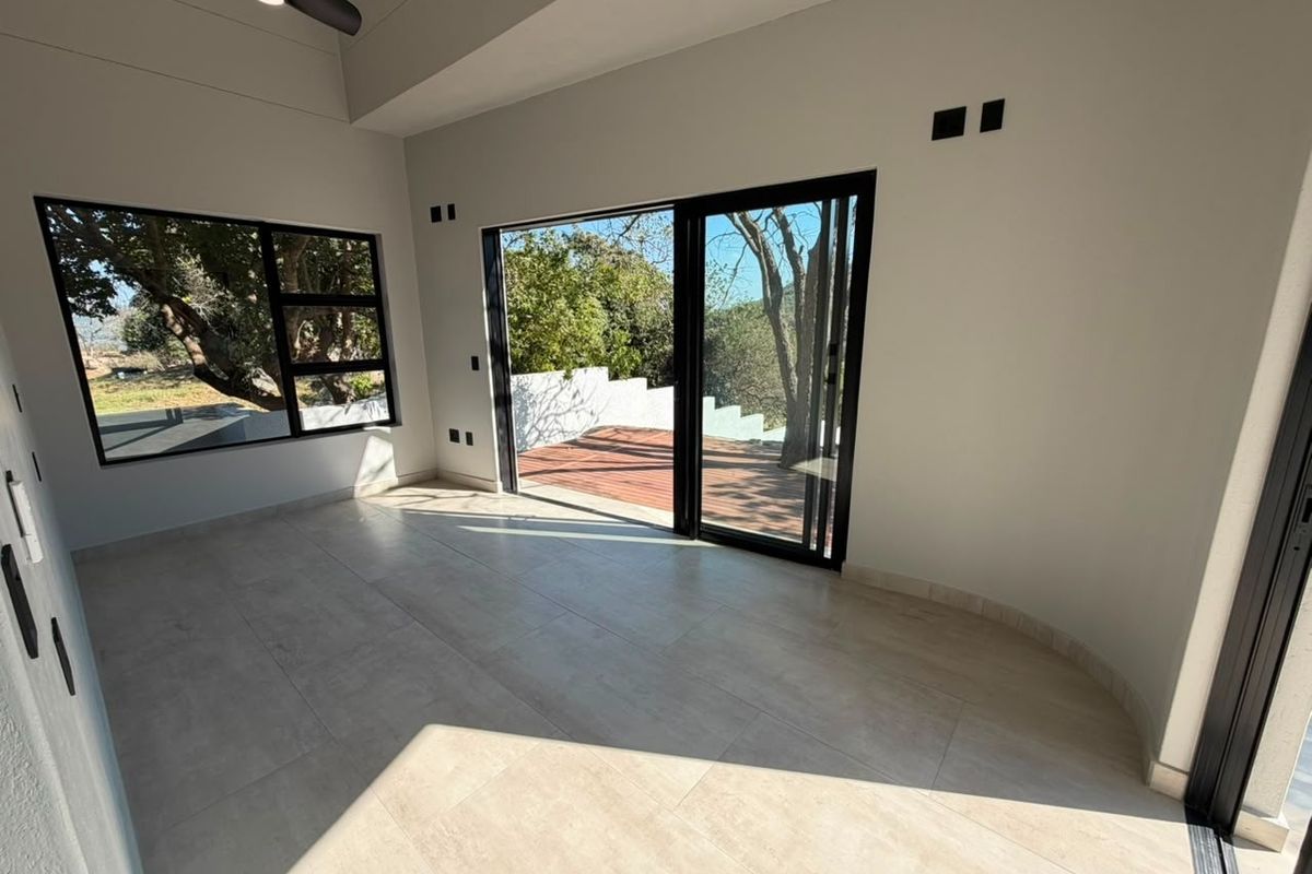 Bright and spacious living area featuring large sliding glass doors that open onto an outdoor deck, complemented by modern tiled flooring and recessed lighting.