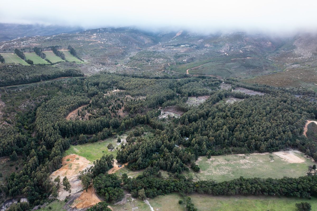 An aerial view of a large, undeveloped residential land parcel featuring dense natural vegetation, cleared areas, and scenic mountain surroundings.