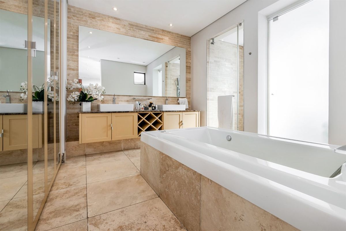 Modern bathroom featuring a double vanity with stone countertop, a built-in bathtub, and a separate glass-enclosed shower with elegant travertine tile finishes.