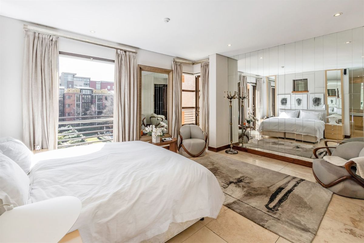 Spacious bedroom featuring large format tiled flooring, a full-height mirrored feature wall, recessed lighting, and direct access to a private balcony.
