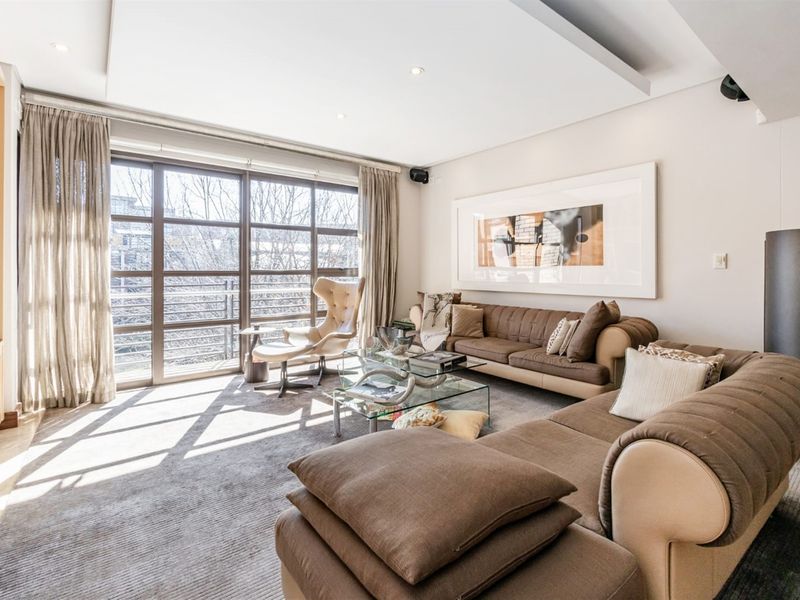 A bright and spacious living room featuring recessed ceiling lighting, plush carpeting, and large floor-to-ceiling windows that provide ample natural light.