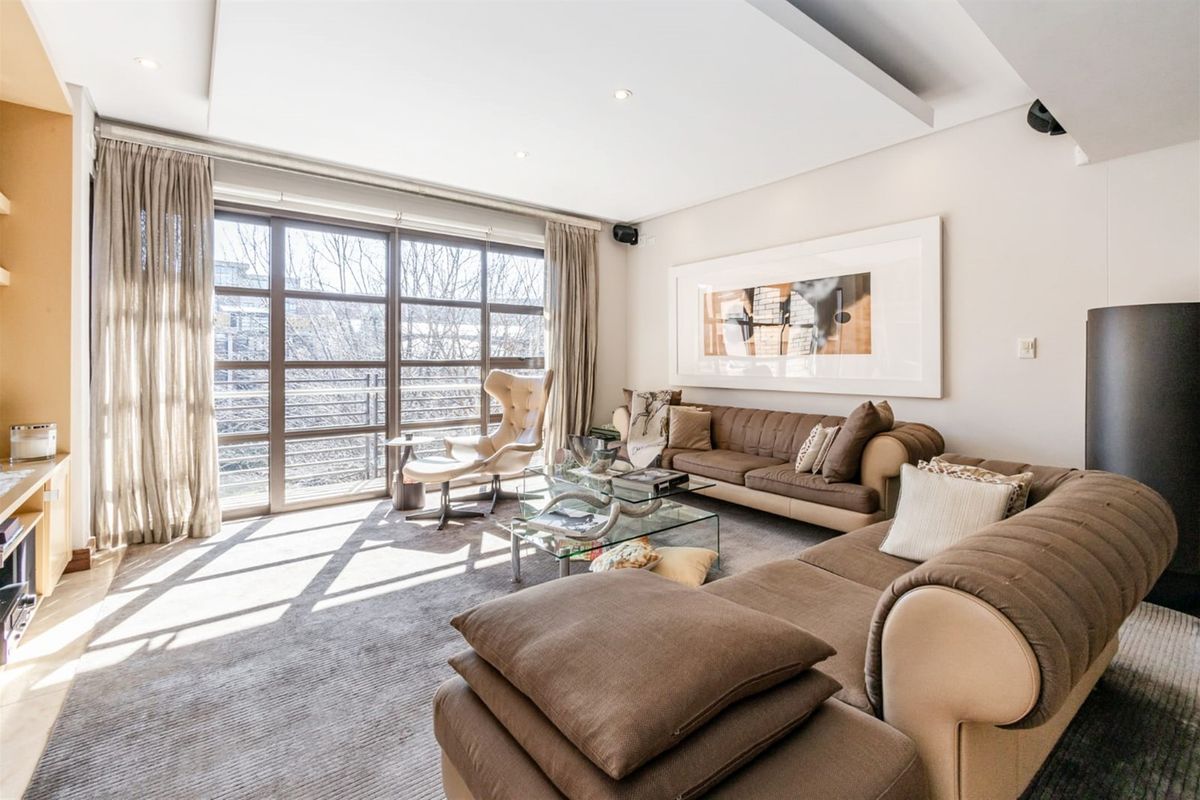 A bright and spacious living room featuring recessed ceiling lighting, plush carpeting, and large floor-to-ceiling windows that provide ample natural light.