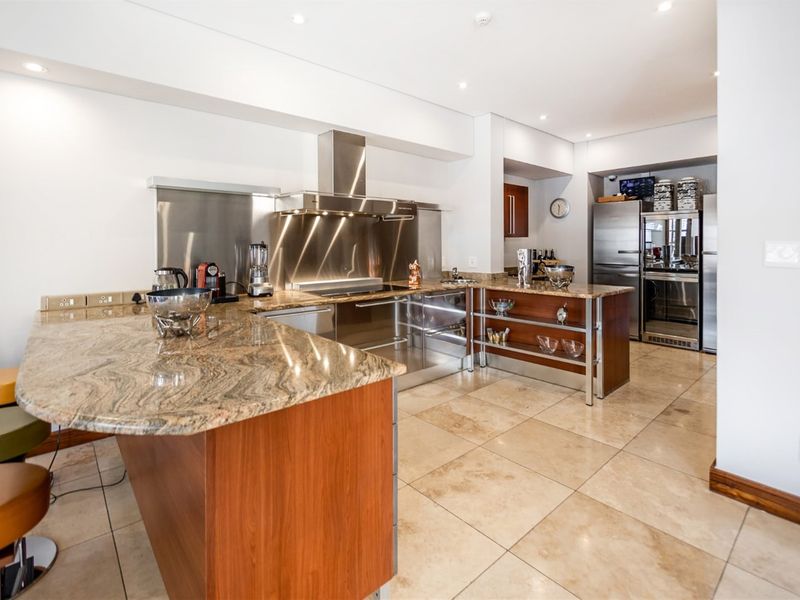 Modern kitchen featuring granite countertops, stainless steel backsplash, integrated appliances, and stone floor tiles with ample cabinetry and recessed lighting.