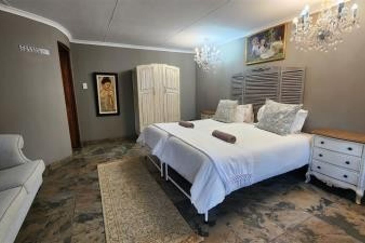A spacious bedroom featuring stone flooring, decorative crystal chandeliers, and a neutral color palette, offering a comfortable and well-maintained sleeping environment.