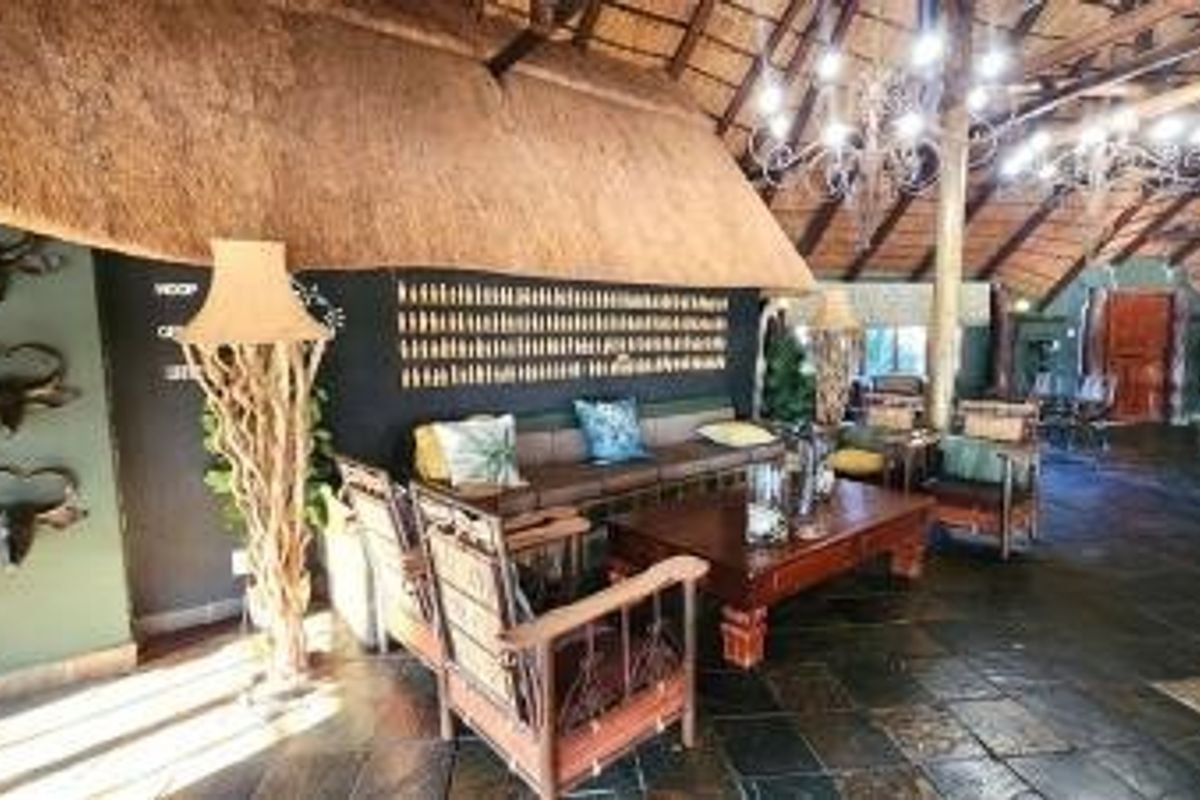Spacious lodge living area featuring a high thatched roof, exposed timber beams, and dark slate flooring, creating a rustic and authentic atmosphere.
