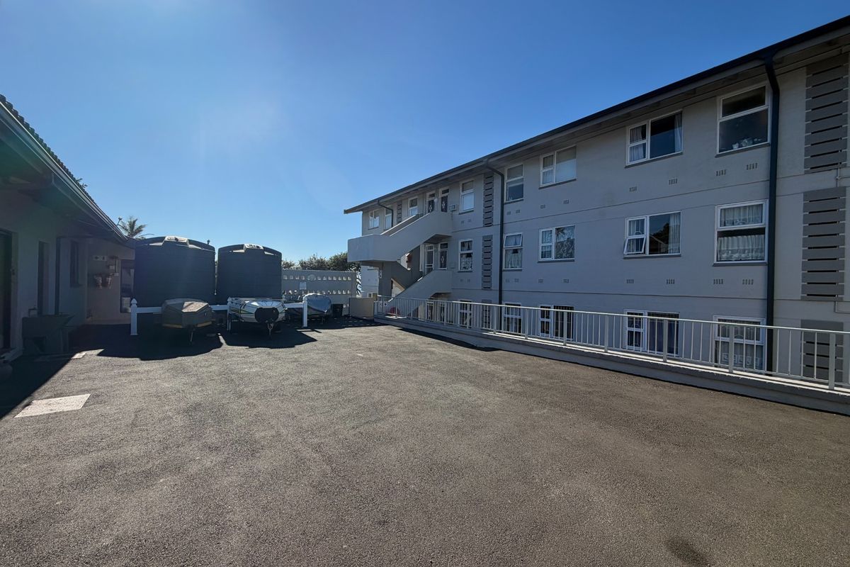 Exterior view of an apartment complex featuring a paved parking area, external staircases, and water storage tanks.