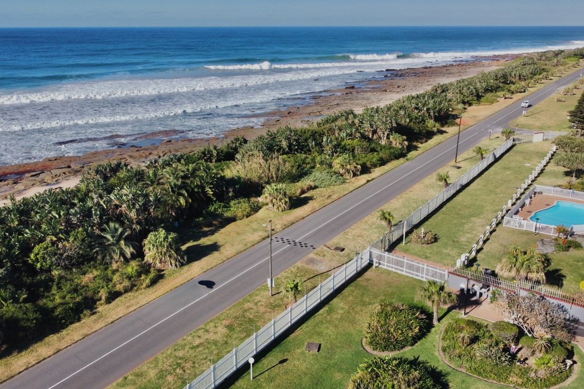 Aerial view of the coastal property, showcasing the swimming pool area, landscaped grounds, and direct proximity to the beach and ocean.