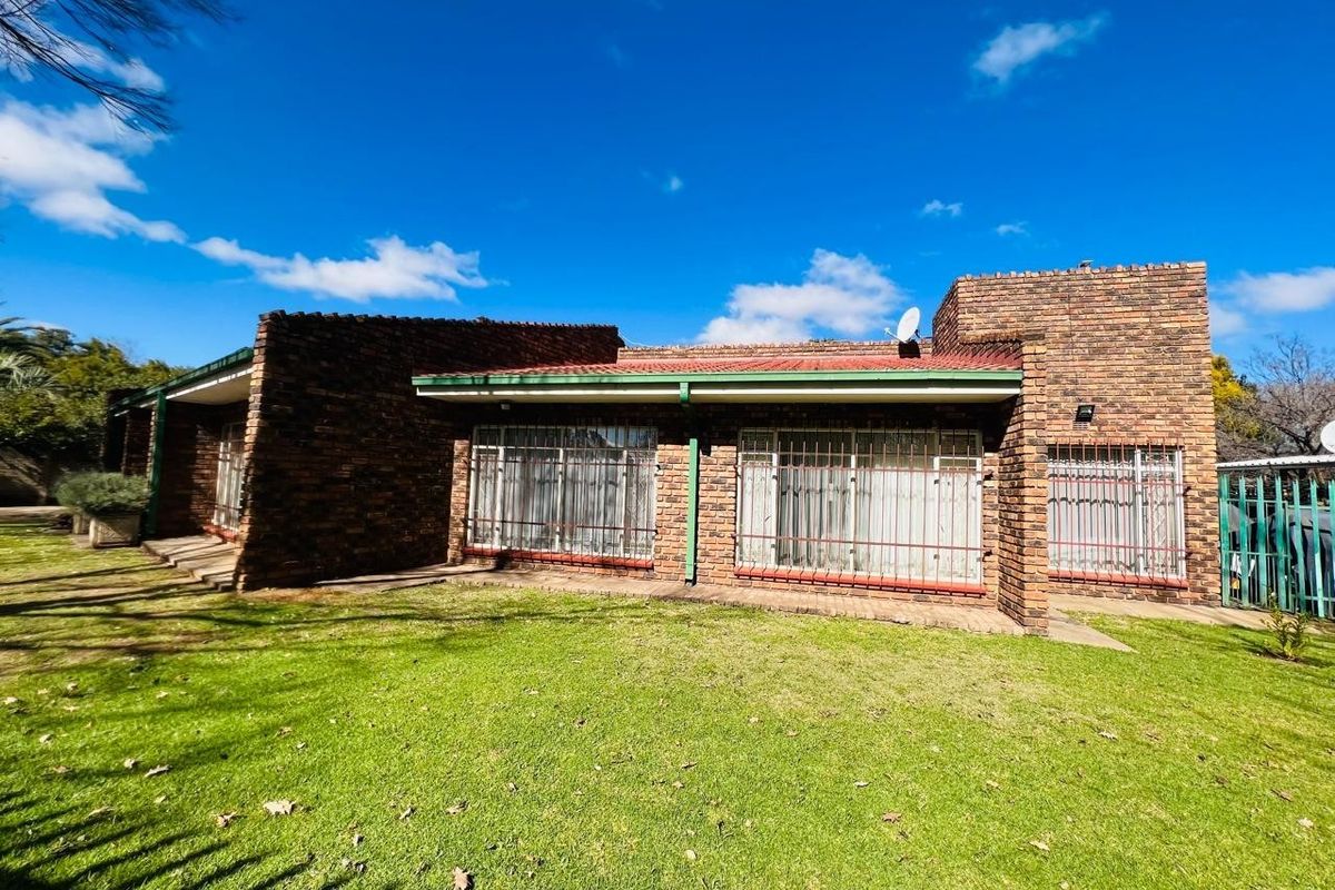 A view of the rear exterior of the house, featuring face-brick walls, a tiled roof, and security bars on the windows, set within a garden.