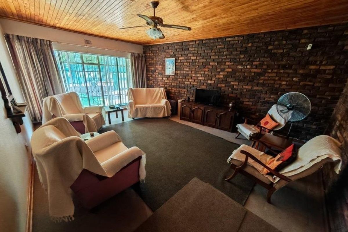 Spacious living room featuring a prominent exposed brick feature wall, timber-clad ceiling, and large windows providing natural light.