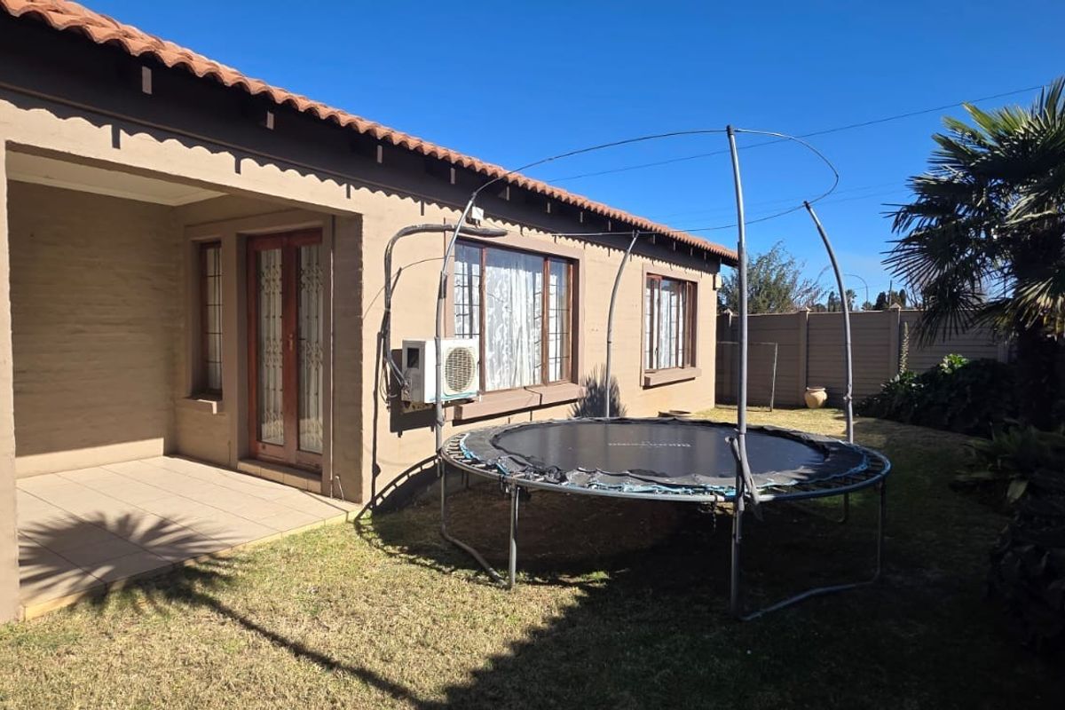 Rear view of the property featuring a covered patio area, tiled flooring, and a private garden space with established landscaping.