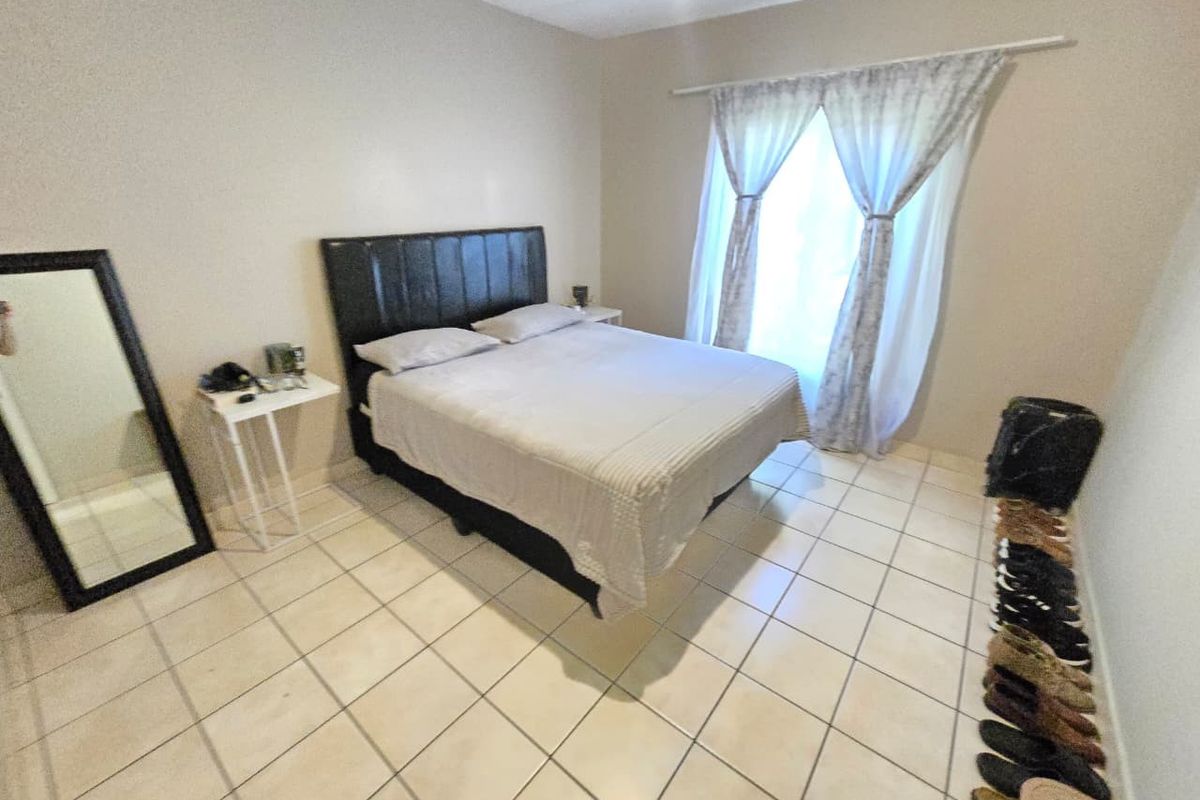 A functional bedroom featuring neutral wall tones, tiled flooring, and a window with curtain treatments.