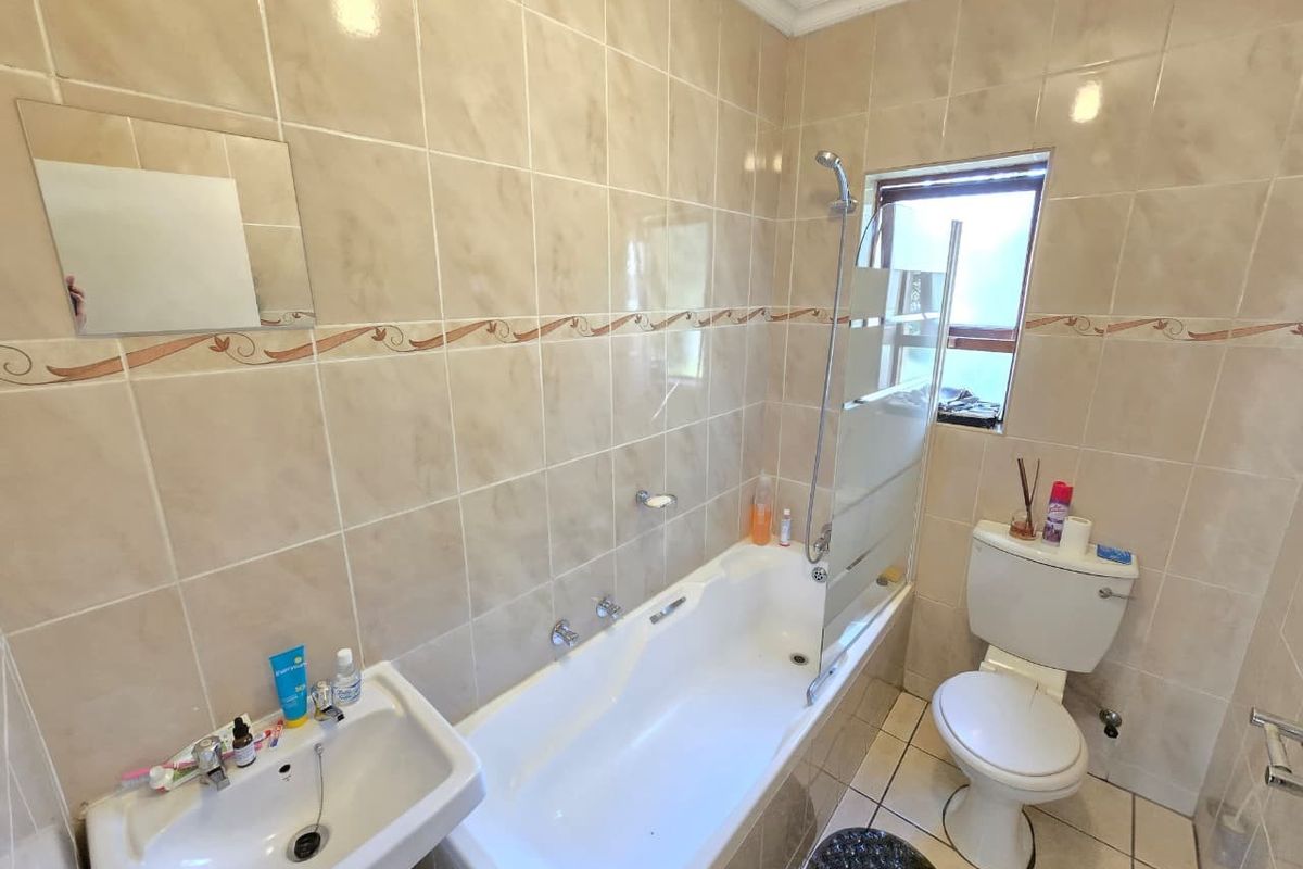 A functional bathroom featuring a bathtub with a shower mixer, glass screen, wall-mounted basin, and a standard toilet with full-height wall tiling.