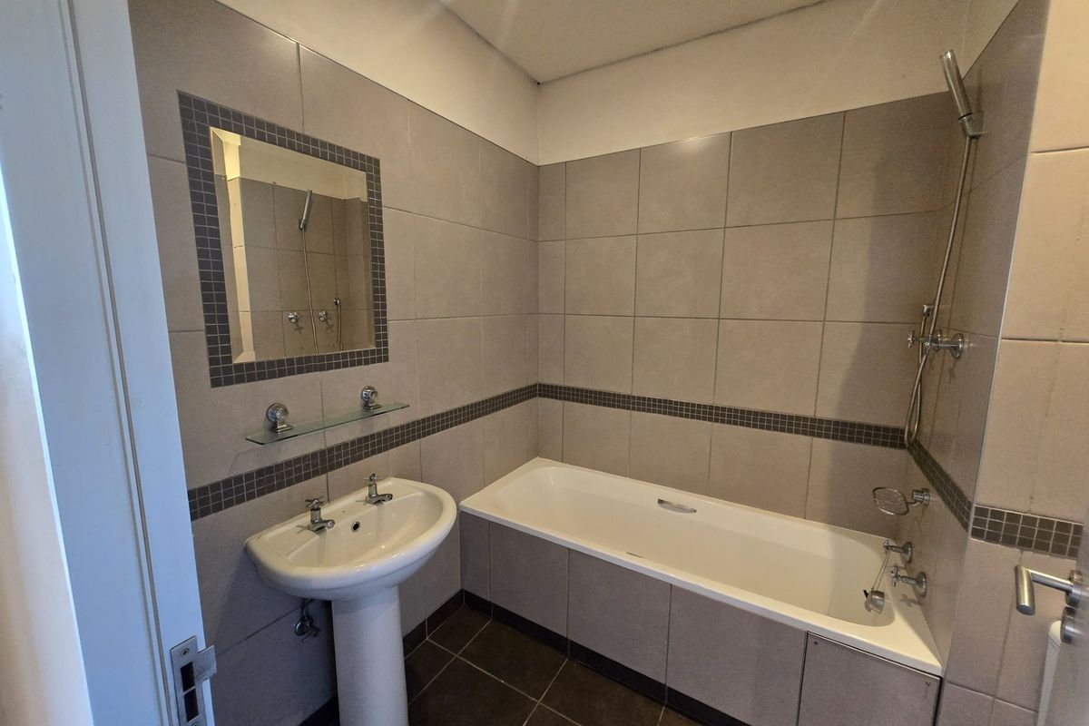A functional bathroom featuring a pedestal basin, a built-in bathtub with shower attachment, and neutral wall tiling with decorative mosaic accents.