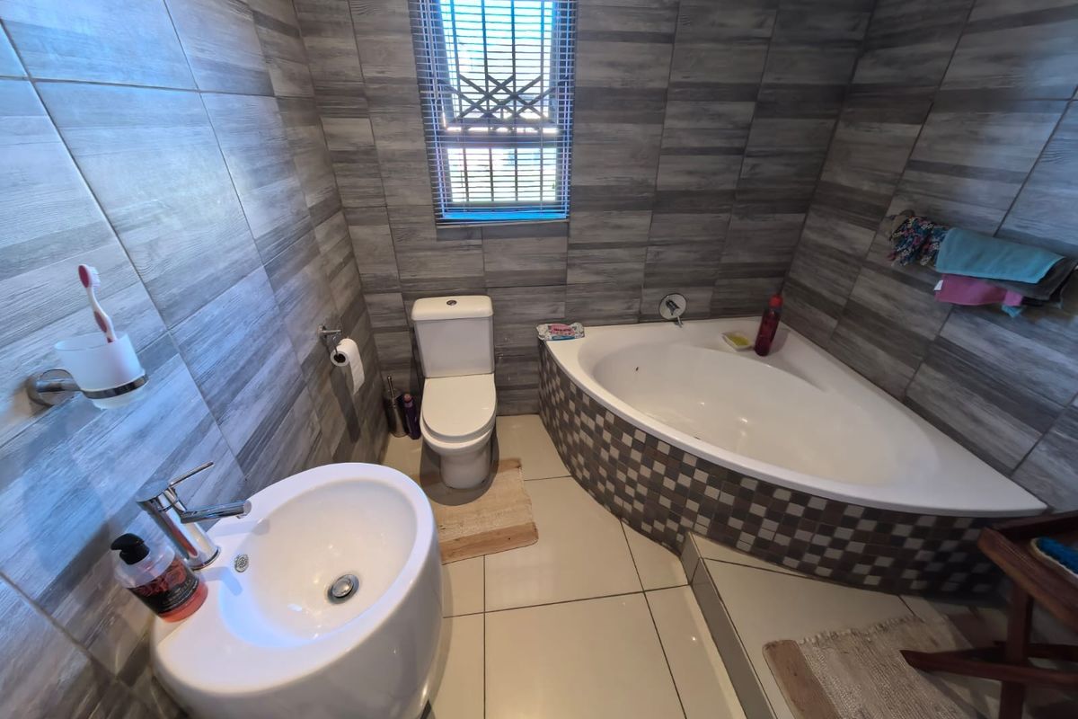 A modern bathroom featuring a corner bathtub with mosaic tiling, a pedestal basin, and a toilet, finished with grey wood-look wall tiles.