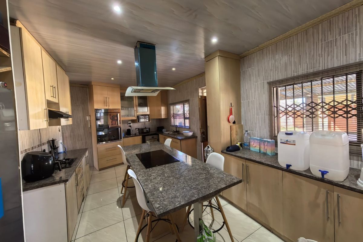 Modern kitchen featuring light wood cabinetry, granite countertops, a central island with a built-in hob, and a stainless steel extractor fan.