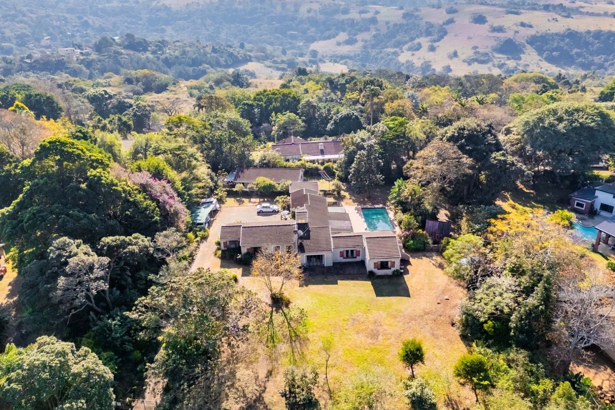 Aerial view of a residential property featuring a swimming pool, expansive garden, and surrounding lush landscape.