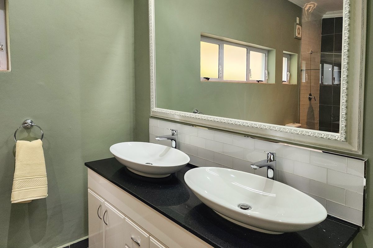 A modern bathroom featuring a double vanity with vessel sinks, black granite countertop, white subway tile backsplash, and a large framed wall mirror.