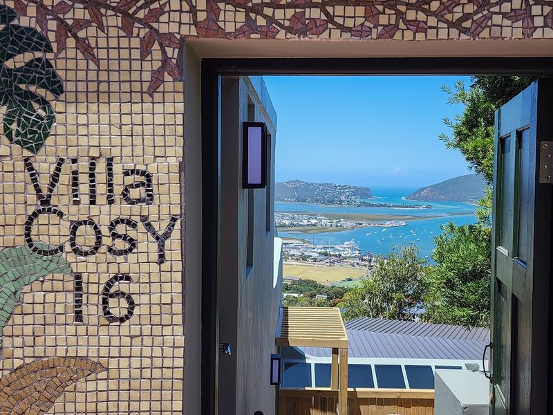 A framed view of the coastal lagoon and surrounding landscape, seen through an open doorway featuring decorative mosaic tile work.