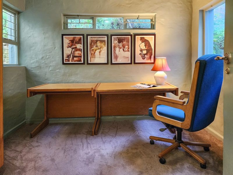 A functional home office space featuring textured walls, carpeted flooring, and a high-level horizontal window providing natural light.