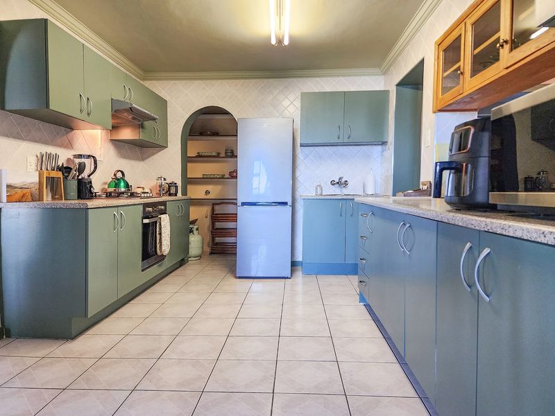A functional kitchen featuring sage green cabinetry, tiled countertops, a built-in oven, and an adjacent arched pantry area with shelving.