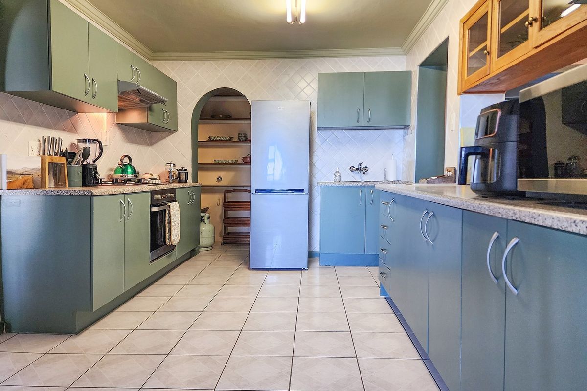 A functional kitchen featuring sage green cabinetry, tiled countertops, a built-in oven, and an adjacent arched pantry area with shelving.