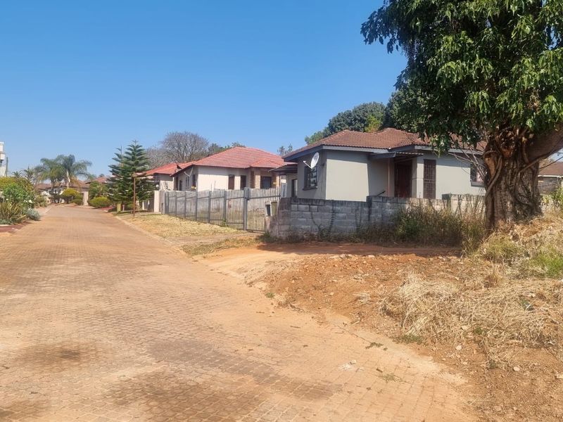 A street view of a residential neighborhood featuring paved roads, perimeter fencing, and established housing in a suburban setting.