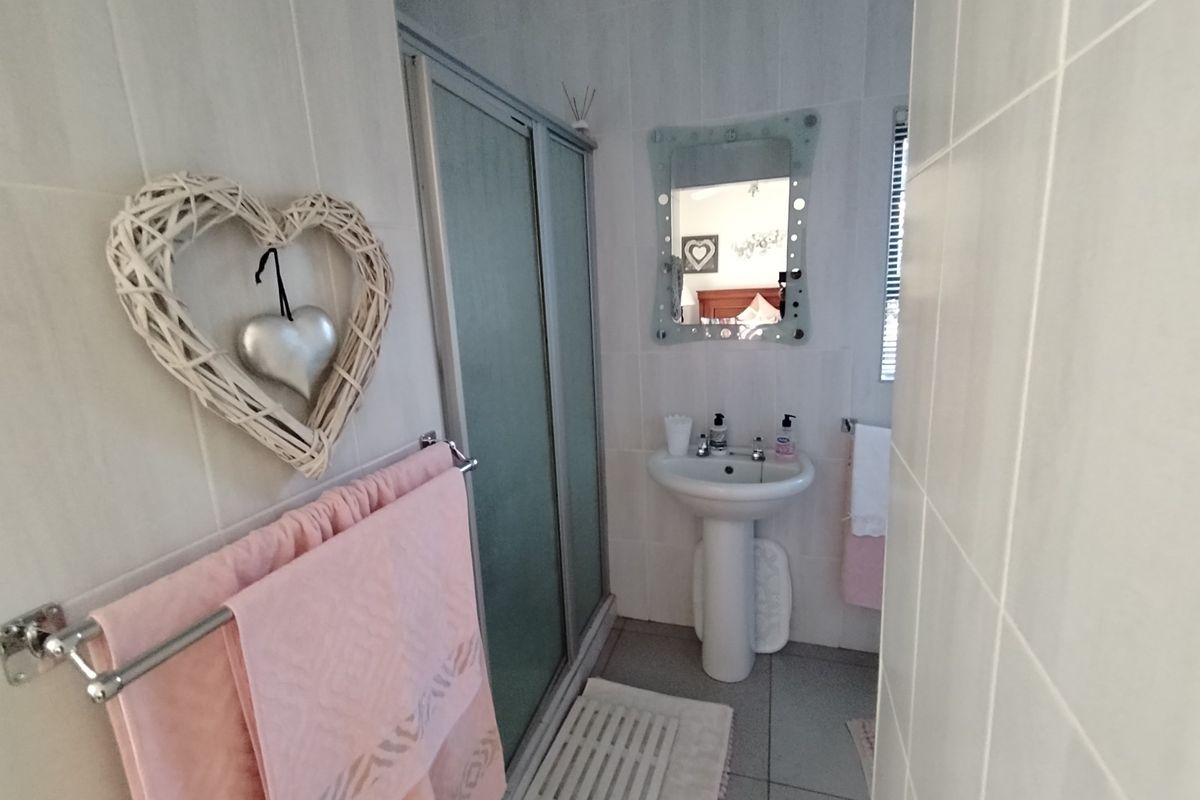 A functional bathroom featuring a pedestal sink, a glass-enclosed shower, and neutral wall tiling.