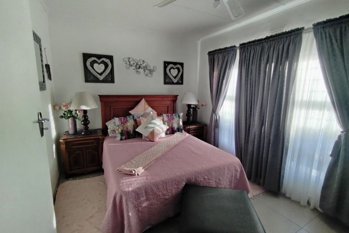 A well-maintained bedroom featuring tiled flooring, a ceiling fan, and large windows with layered curtains.
