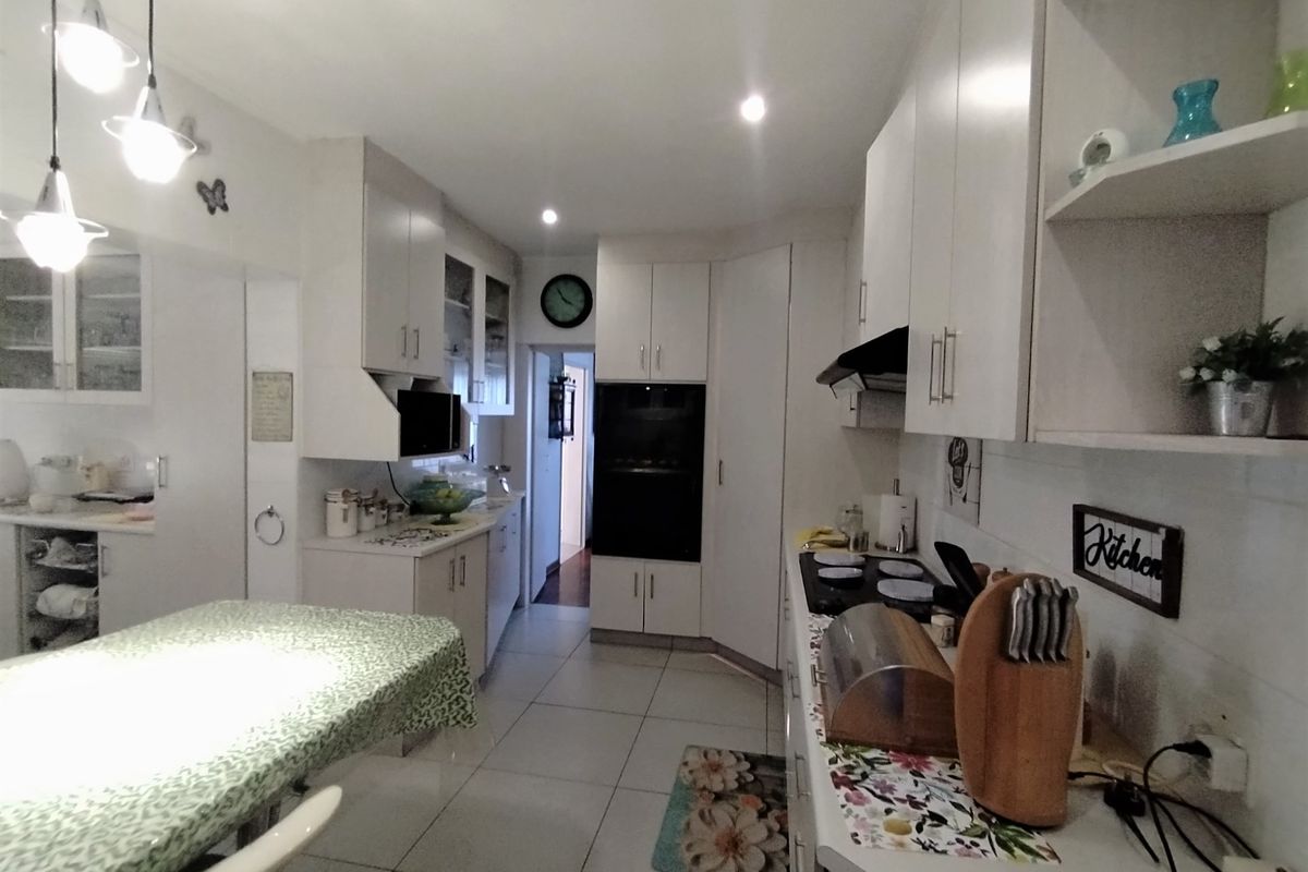 A functional kitchen featuring white cabinetry, built-in oven, hob, extractor fan, and tiled flooring with ample storage space.