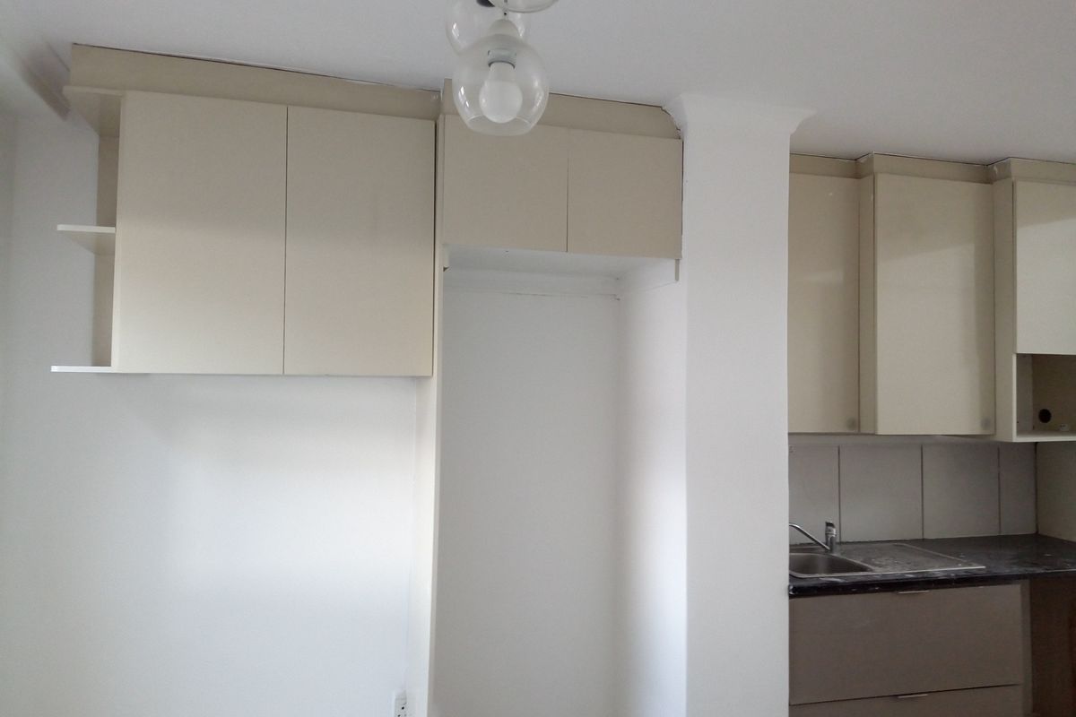 A compact kitchen area featuring neutral-toned cabinetry, a stainless steel sink, and a dedicated space for a refrigerator.