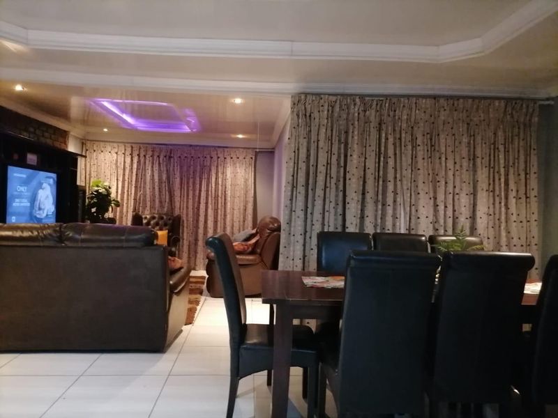 An open-plan living and dining area featuring tiled flooring, recessed ceiling lighting, and a built-in media wall unit.