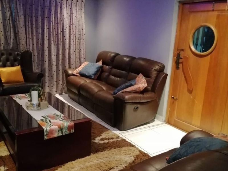 A living room featuring a recessed ceiling with integrated purple LED lighting, tiled flooring, and a solid timber door with a circular porthole window.