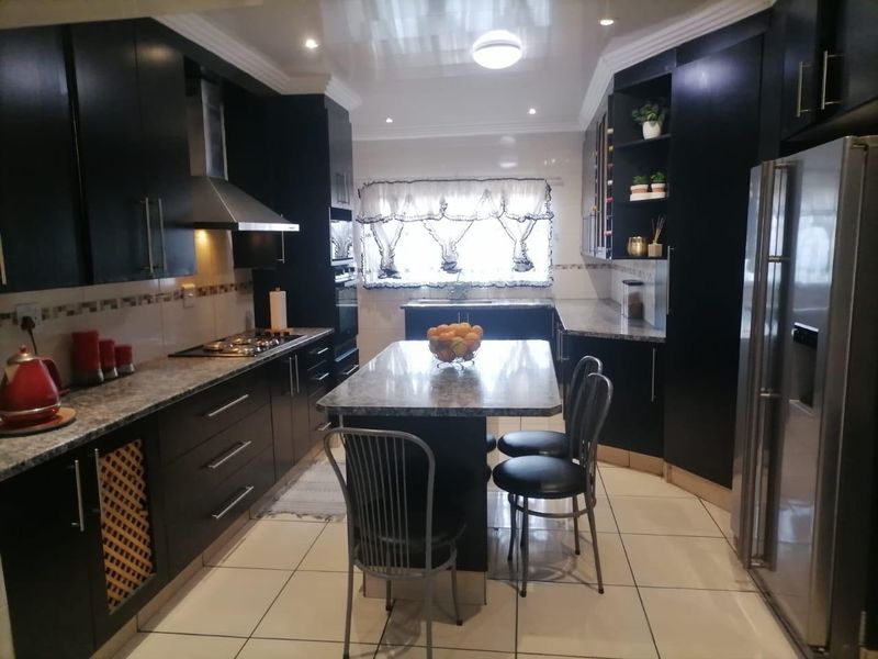 Modern kitchen featuring dark cabinetry, granite countertops, a central island, stainless steel extractor fan, and tiled flooring.